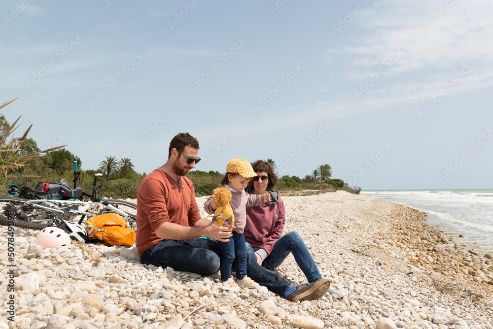 Couple with her little daughter at a pebble beach with their bicycles behind them. Low-footprint transportation.
