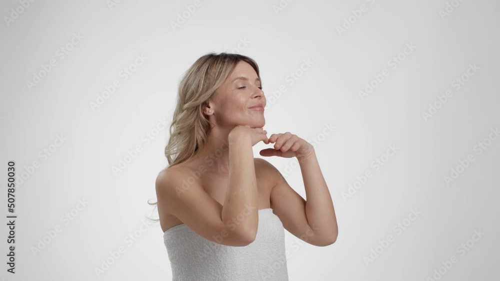 Anti aging body care. Beautiful middle aged lady wrapped in towel making skin lifting self massage for her chin and neck Anti aging body care. Beautiful middle aged lady wrapped in towel making skin lifting self massage for her chin and neck
