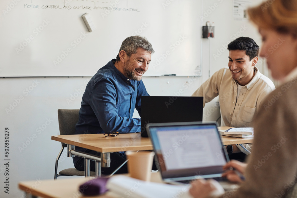 Smiling teacher and student looking at laptop while sitting in classroom Smiling teacher and student looking at laptop while sitting in classroom