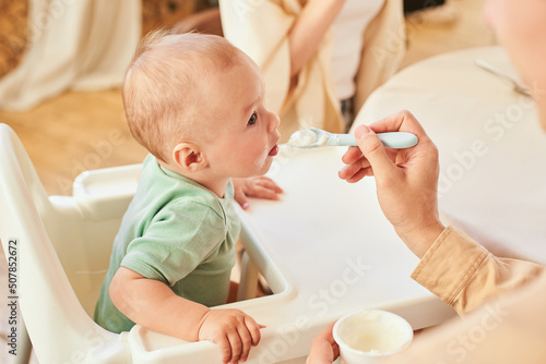 A dad spoons his toddler with yogurt.