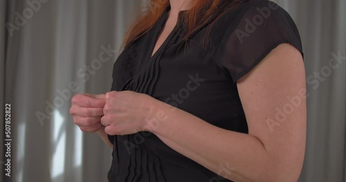 Close up of young brunette woman unbuttoning her black top moving sideways through the frame. Slow motion.
