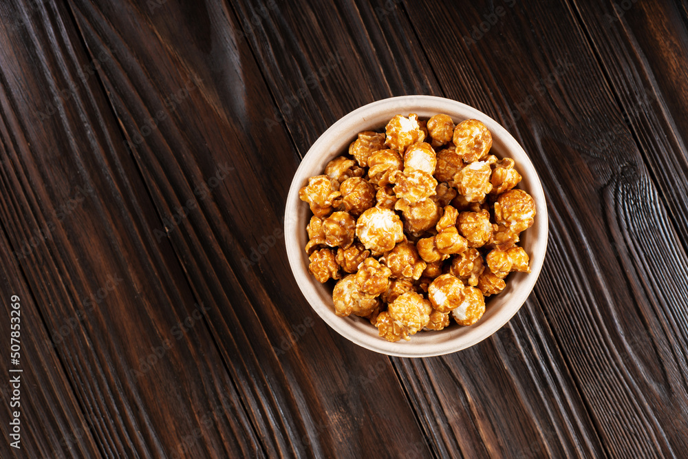 Caramelized popcorn in paper bucket on wooden kitchen table flat lay