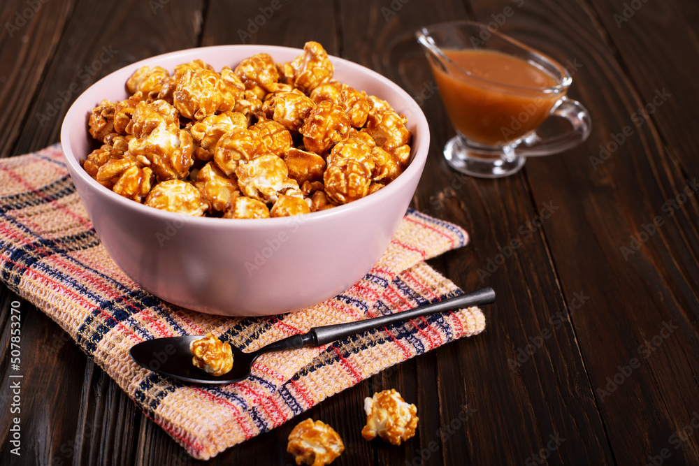 Clay bowl with caramel popcorn on wooden background
