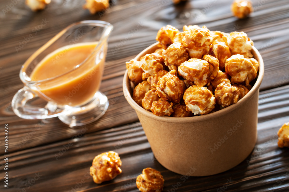 Caramelized popcorn in paper bucket on wooden table