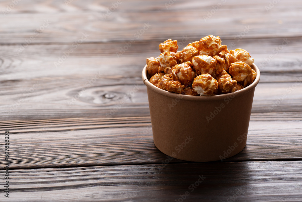 Caramelized popcorn in paper bucket on wooden kitchen table