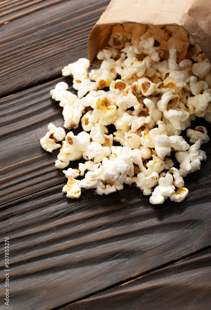 Popped corn snack in paper bag on wooden table closeup