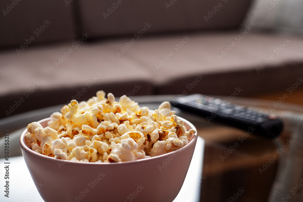 Bowl with popcorn and tv remote control on glass table near sofa