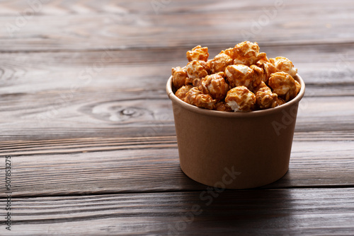 Obraz na płótnie Caramelized popcorn in paper bucket on wooden kitchen table w salonie