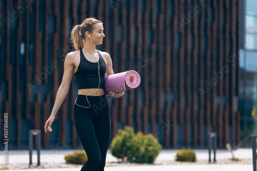Girl with ponytail going  waking with rolled yoga mat.