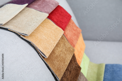 Catalog of colorful fabric samples on grey sofa, closeup