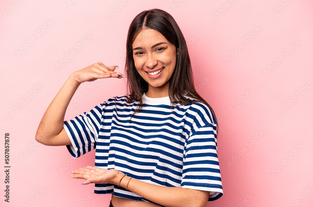 Young hispanic woman isolated on pink background holding something little with forefingers, smiling and confident. Young hispanic woman isolated on pink background holding something little with forefingers, smiling and confident.
