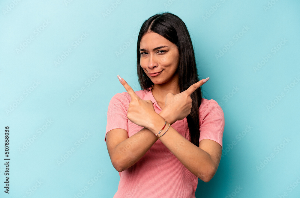 Young hispanic woman isolated on blue background points sideways, is trying to choose between two options.