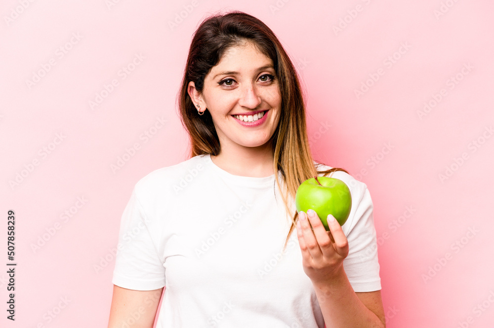 Young caucasian woman holding an apple isolated on pink background happy, smiling and cheerful. Young caucasian woman holding an apple isolated on pink background happy, smiling and cheerful.