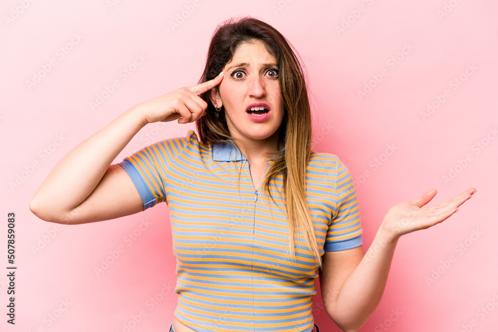 Young caucasian woman isolated on pink background holding and showing a product on hand. Young caucasian woman isolated on pink background holding and showing a product on hand.