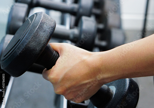 Close up of hand holding dumbbell in fitness. Concept of exercise, healthy and lose weight.