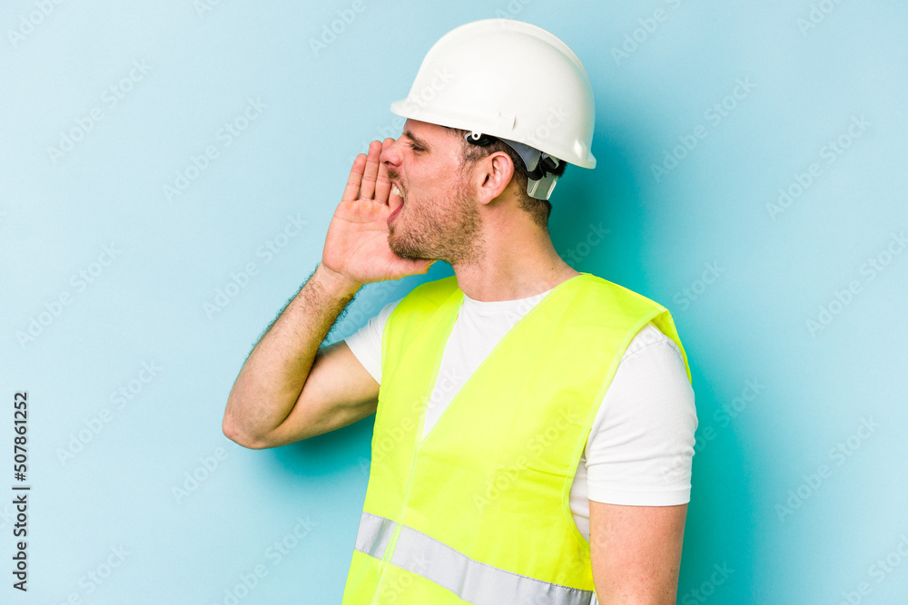 Young laborer caucasian man isolated on blue background shouting and holding palm near opened mouth.