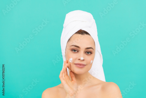 cheerful young girl apply face cream on blue background