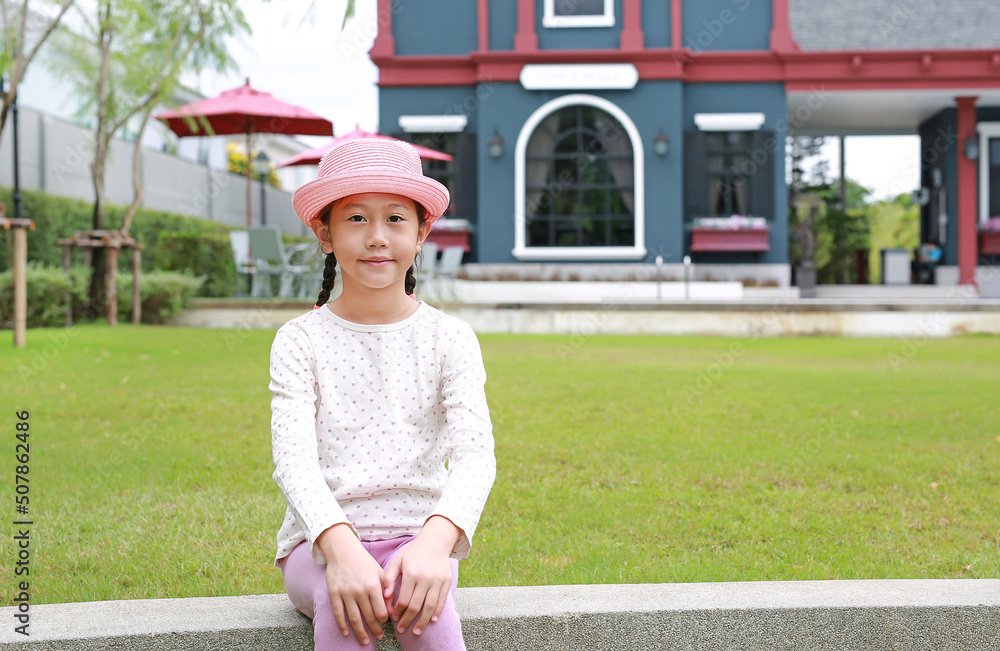 Portrait of Asian young girl child wearing pink straw hat sitting in the garden.