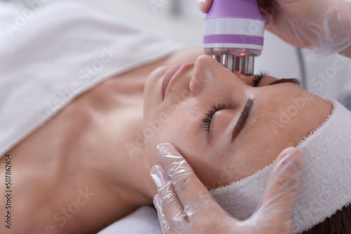 A young woman undergoing a facial radiofrequency face lift treatment. Facial skin care treatment, anti-aging facial rejuvenation. Beauty and dermatology concept. photo