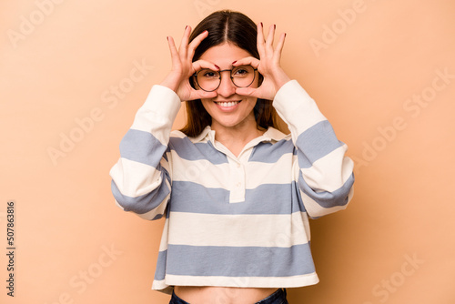 Young hispanic woman isolated on beige background showing okay sign over eyes