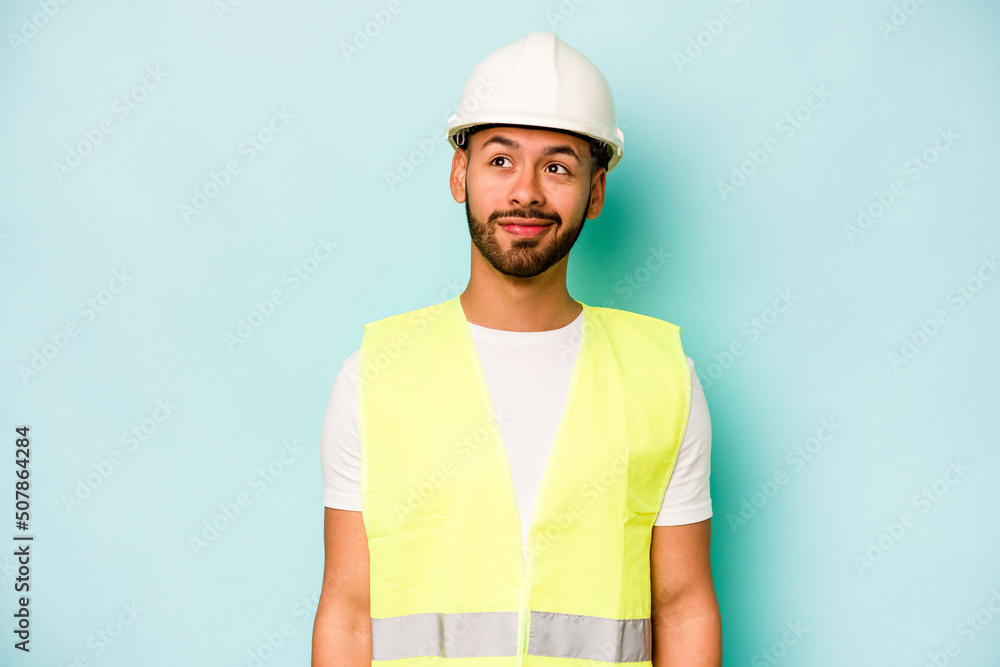 Young laborer hispanic man isolated on blue background dreaming of achieving goals and purposes