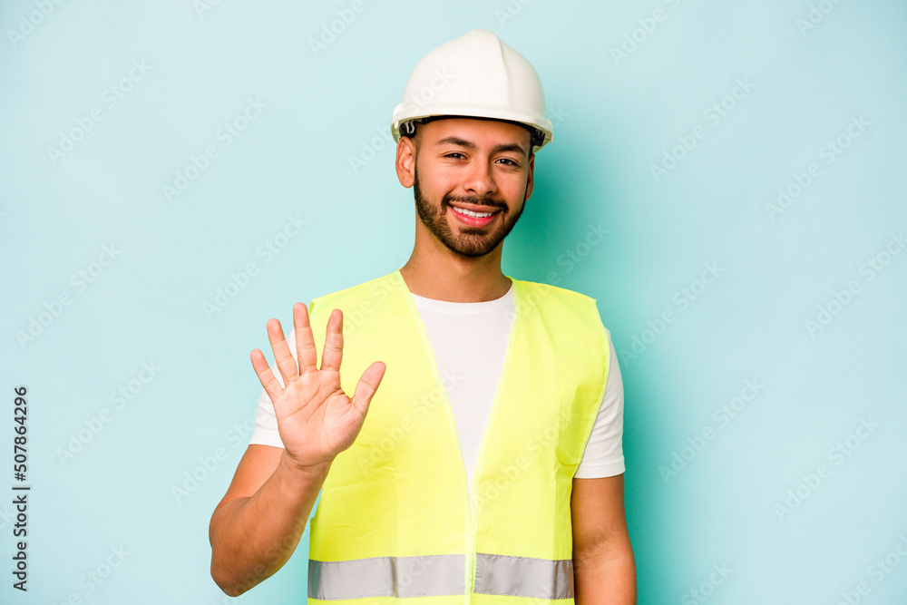 Young laborer hispanic man isolated on blue background smiling cheerful showing number five with fingers.