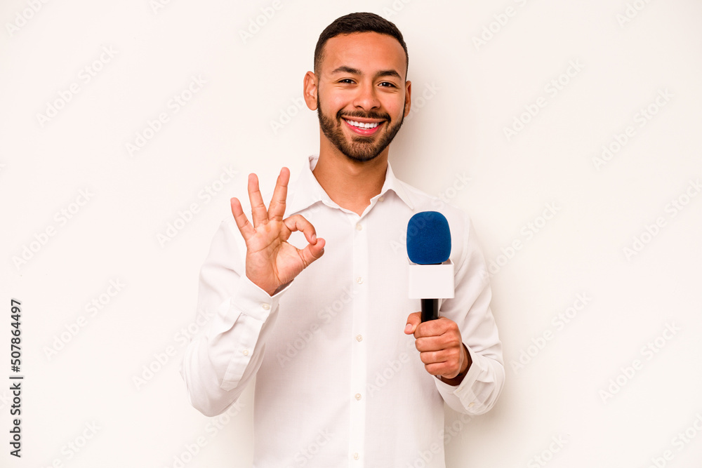 Young hispanic TV presenter isolated on blue background cheerful and confident showing ok gesture. Young hispanic TV presenter isolated on blue background cheerful and confident showing ok gesture.