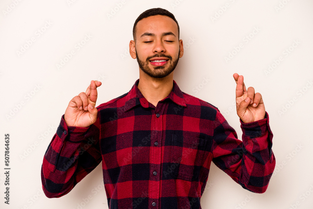 Naklejka premium Young hispanic man isolated on white background crossing fingers for having luck