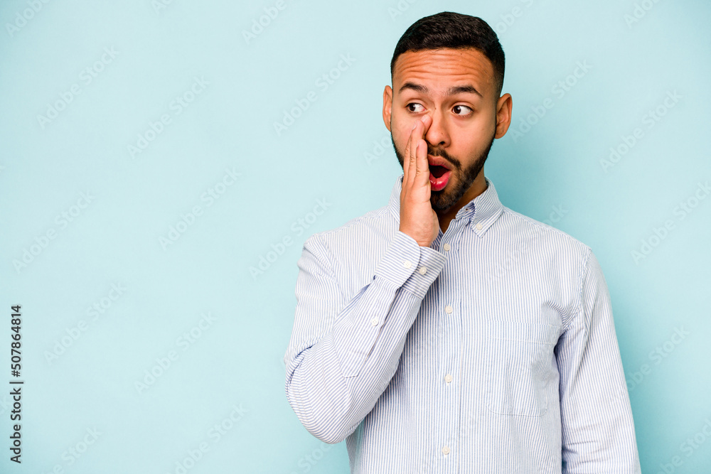 Young hispanic man isolated on blue background is saying a secret hot braking news and looking aside Young hispanic man isolated on blue background is saying a secret hot braking news and looking aside