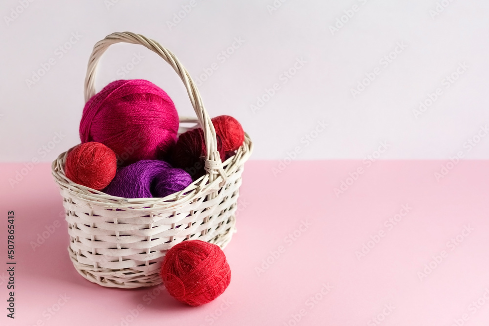 Pink and red balls of thread in a basket on a pink background, Hobby