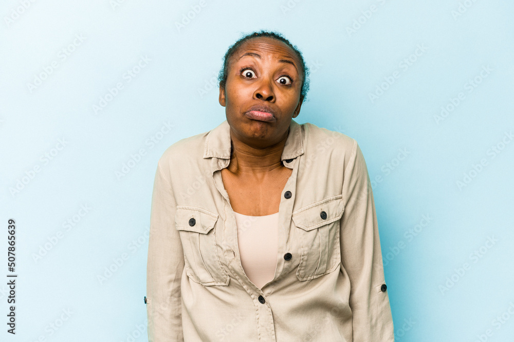 Young african american woman isolated on blue background shrugs shoulders and open eyes confused. Young african american woman isolated on blue background shrugs shoulders and open eyes confused.