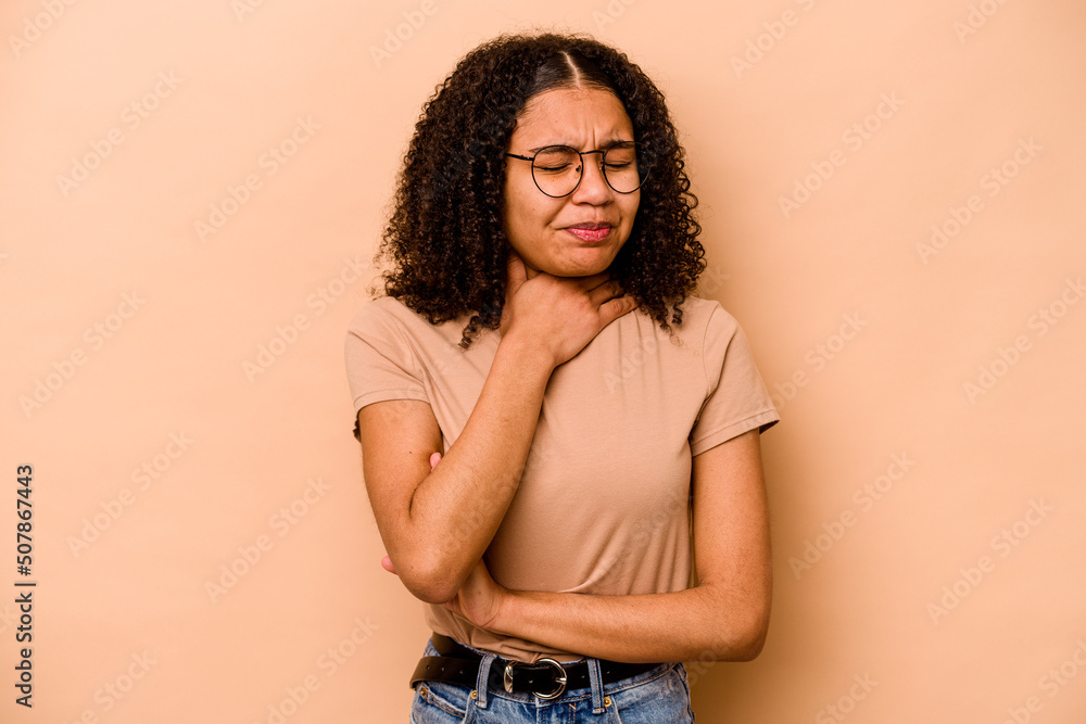 Young African American woman isolated on beige background suffers pain in throat due a virus or infection. Young African American woman isolated on beige background suffers pain in throat due a virus or infection.
