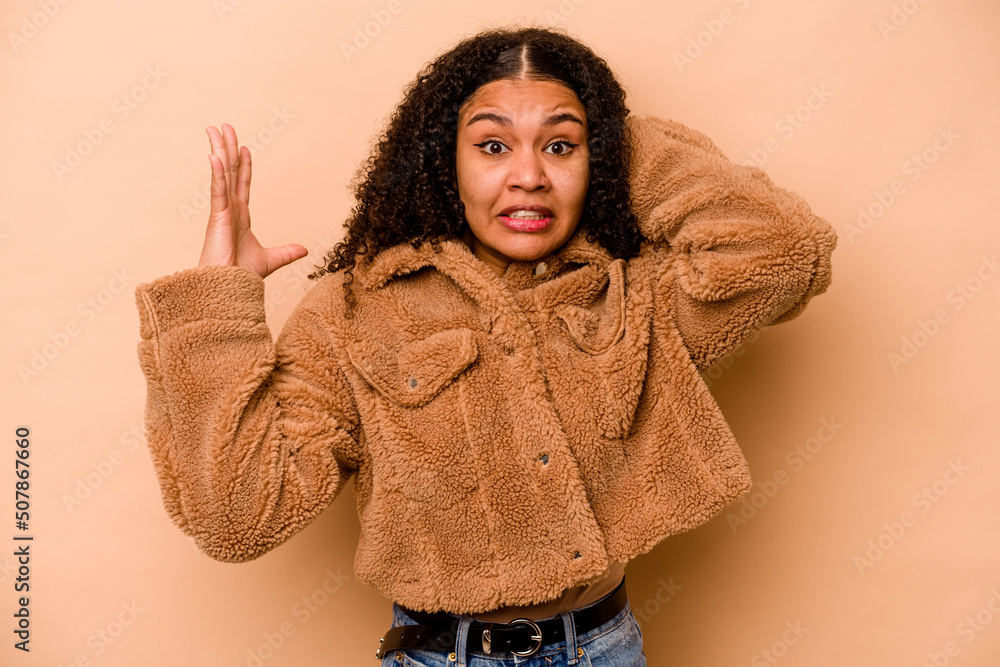 Young African American woman isolated on beige background screaming with rage. Young African American woman isolated on beige background screaming with rage.