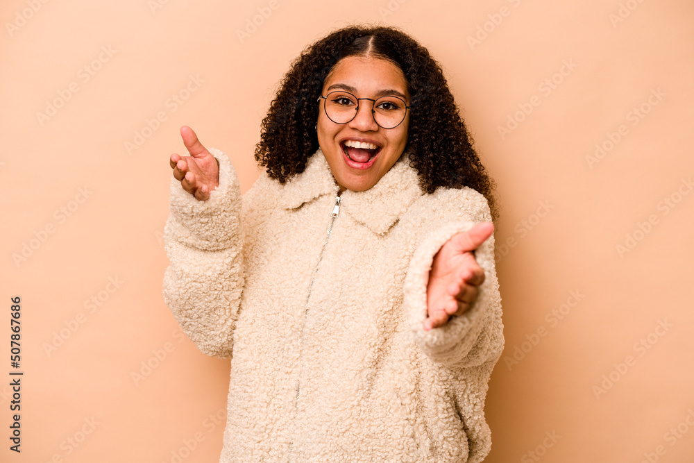 Young African American woman isolated on beige background feels confident giving a hug to the camera. Young African American woman isolated on beige background feels confident giving a hug to the camera.