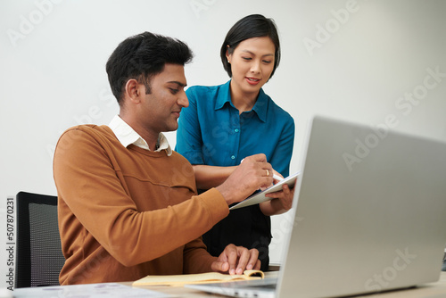 Smiling Indian entrepreneur signing important documant in hands of his assistant photo