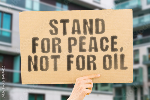 The phrase " Stand for peace, not for oil " is on a banner in men's hands with blurred background. Expense. Growth. Armor. Enemy. Defense. Fueling. Pipe. Warrior. Petrol. Pump. Warfare. Pipeline