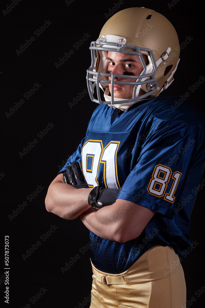 Young football player standing with arms folded looking tough on dark background