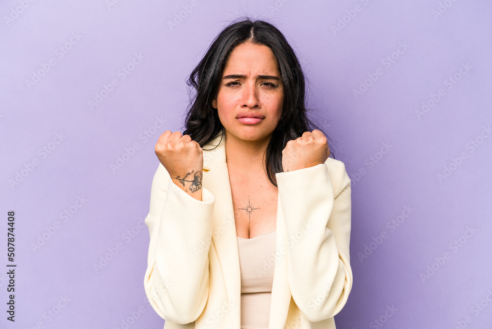 Young hispanic woman isolated on purple background showing fist to camera, aggressive facial expression. Young hispanic woman isolated on purple background showing fist to camera, aggressive facial expression.