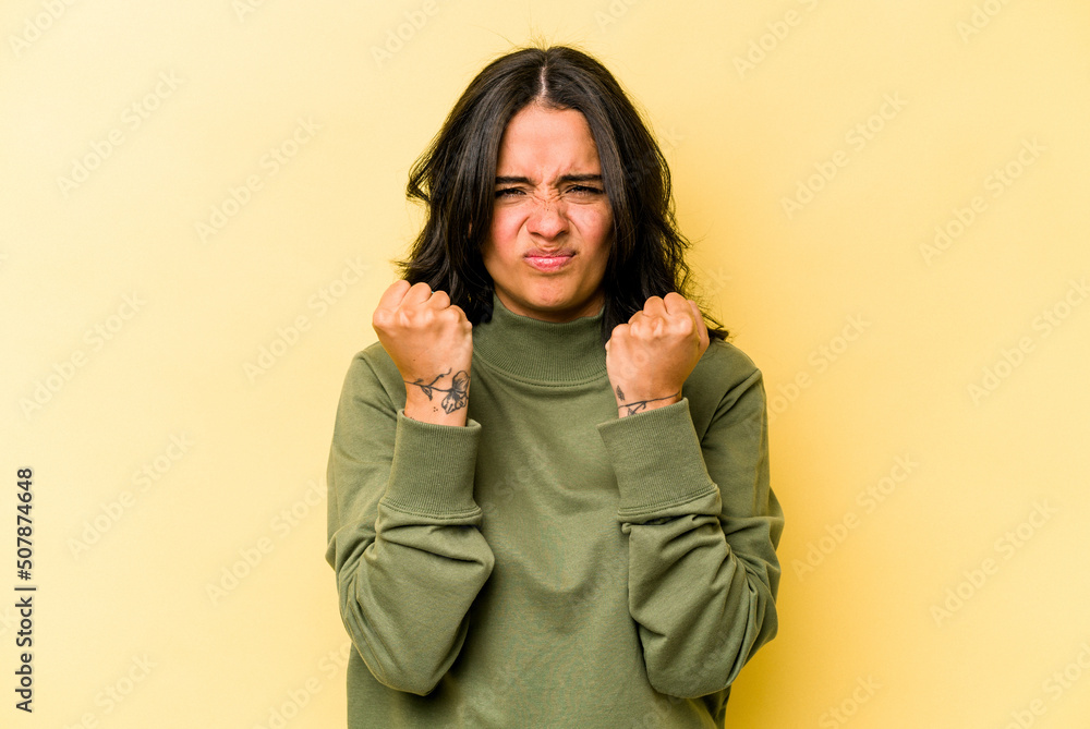 Young hispanic woman isolated on yellow background showing fist to camera, aggressive facial expression. Young hispanic woman isolated on yellow background showing fist to camera, aggressive facial expression.