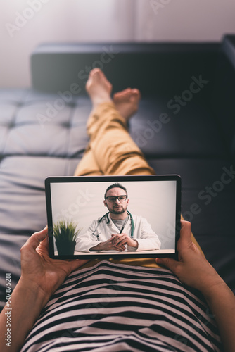 Woman lying on a sofa and talking with a doctor online using digital tablet. Telemedicine concept.