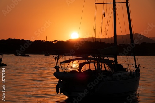 Fototapeta Naklejka Na Ścianę i Meble -  A white sailboat sails on the sea with an orange sunset