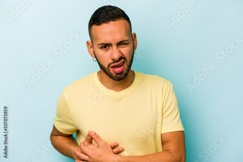 Young hispanic man isolated on blue background having a liver pain, stomach ache.