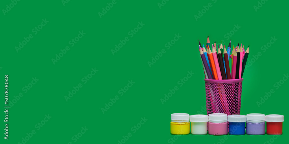 Back to school Education concept. Painting supplies, colorful pencils and plastic jars with paint of different colors for children's creativity on green background. Materials for drawing, banner