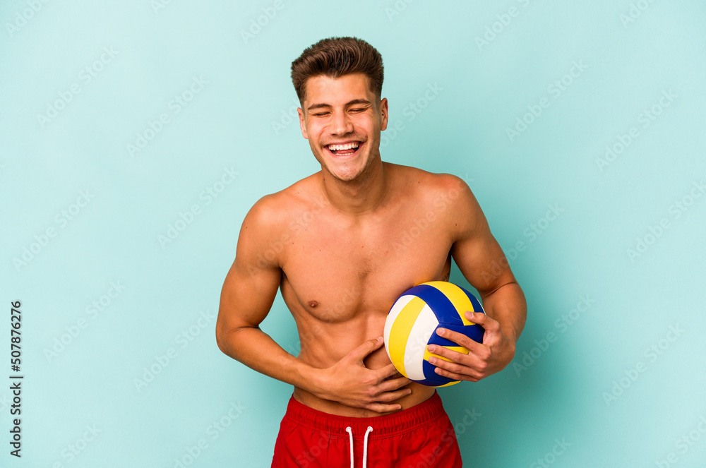 Young caucasian man playing volley isolated on blue background laughing and having fun.