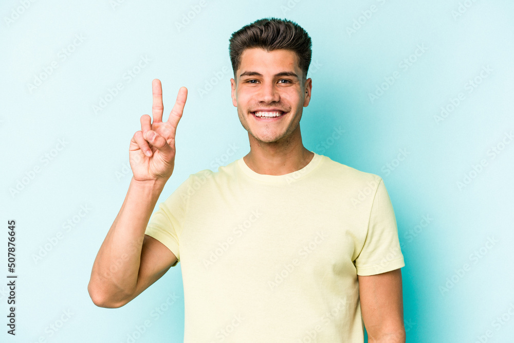 Young caucasian man isolated on blue background showing victory sign and smiling broadly. Young caucasian man isolated on blue background showing victory sign and smiling broadly.