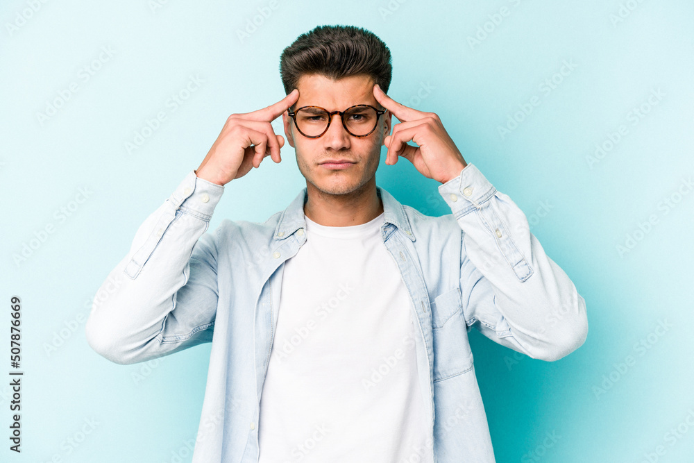 Young caucasian man isolated on blue background focused on a task, keeping forefingers pointing head. Young caucasian man isolated on blue background focused on a task, keeping forefingers pointing head.