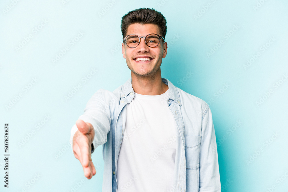 Young caucasian man isolated on blue background stretching hand at camera in greeting gesture. Young caucasian man isolated on blue background stretching hand at camera in greeting gesture.