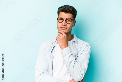 Young caucasian man isolated on blue background suspicious, uncertain, examining you.