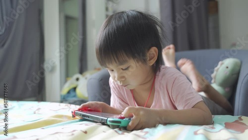 Little boy lying in bed and playing a video game on portable mobile game or mobile phone while spending free time at home