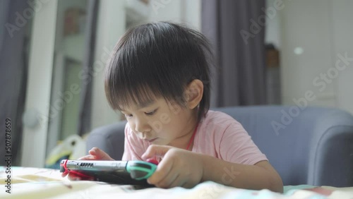 Little boy lying in bed and playing a video game on portable mobile game or mobile phone while spending free time at home